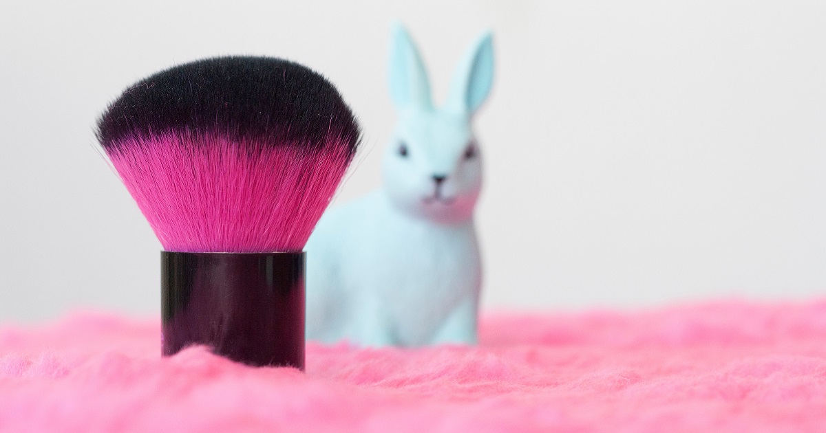 Image shows a pink makeup brush with a small rabbit behind it looking worried.