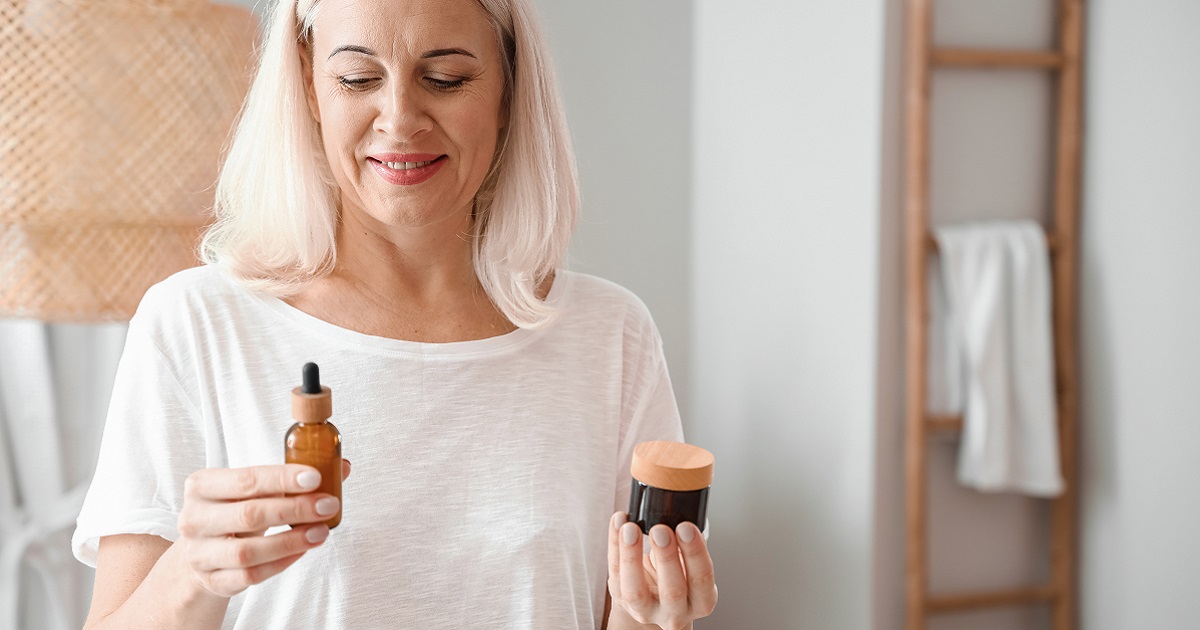 Image shows a woman look at a choice of face cream or serum, one in each hand